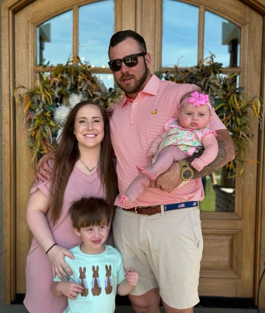 David with his family, all four together outside a wooden doorway