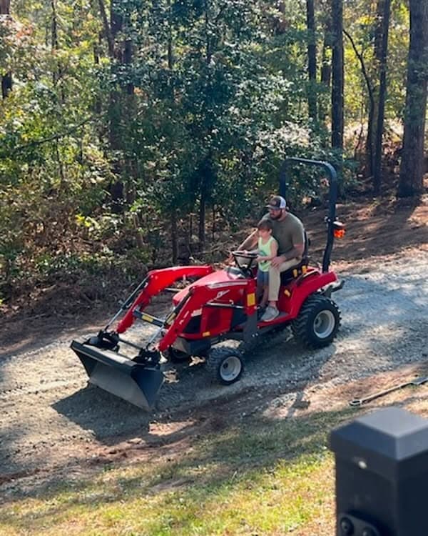 David and his son together on a red tractor beside the woods